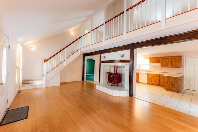 unfurnished living room with light wood-type flooring, a wood stove, a towering ceiling, and stairs