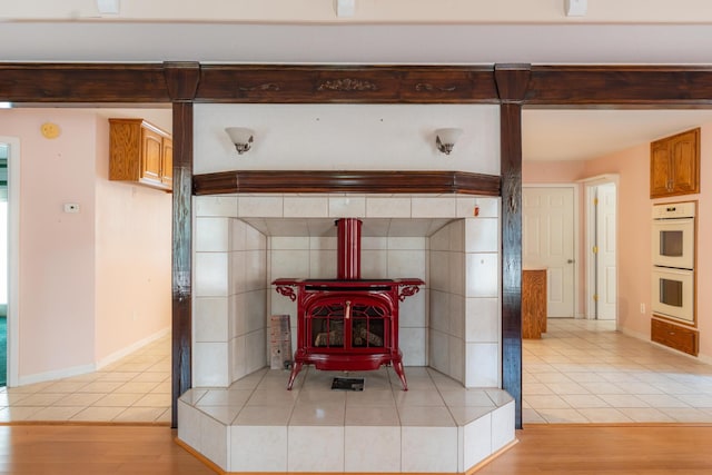 interior details with baseboards, white double oven, wood finished floors, a wood stove, and beam ceiling