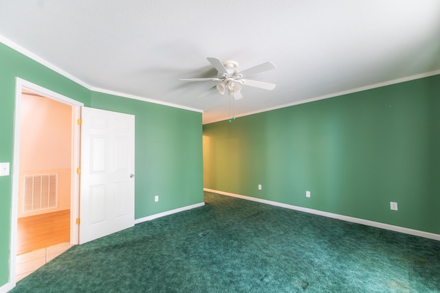 carpeted spare room featuring baseboards, ornamental molding, visible vents, and a ceiling fan