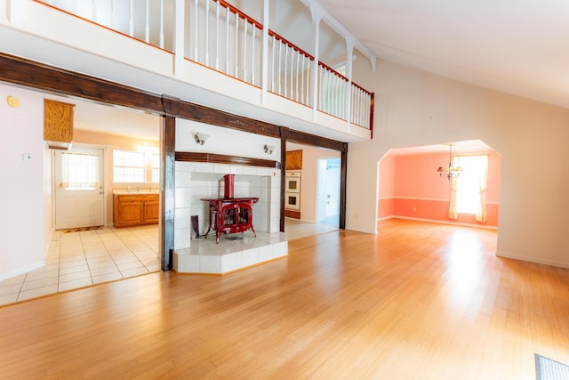 unfurnished living room with a chandelier, high vaulted ceiling, light wood finished floors, and a wood stove