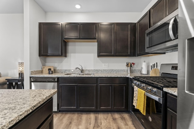 kitchen with light wood finished floors, light stone counters, stainless steel appliances, and a sink