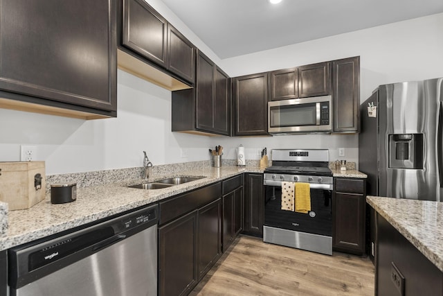 kitchen with light stone counters, appliances with stainless steel finishes, dark brown cabinets, light wood-type flooring, and a sink