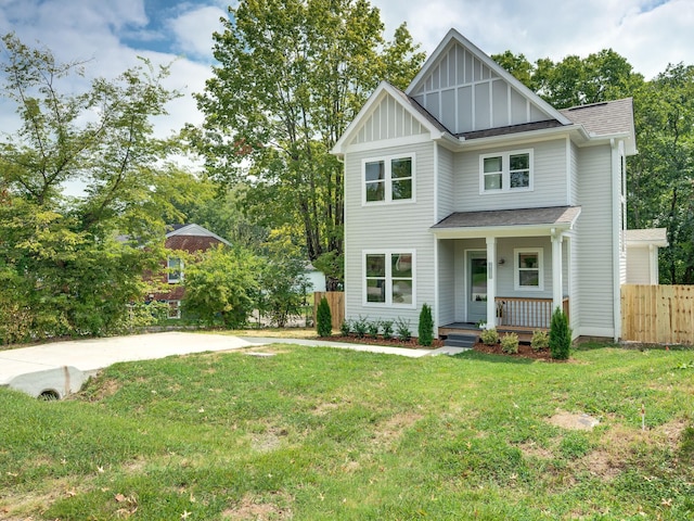 view of front of home with board and batten siding, fence, roof with shingles, a front yard, and covered porch