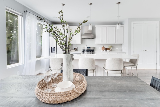 interior space featuring stainless steel gas range oven, a kitchen bar, light countertops, wall chimney exhaust hood, and a kitchen island with sink