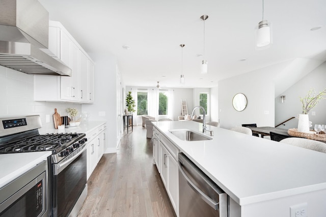 kitchen with backsplash, open floor plan, appliances with stainless steel finishes, wall chimney exhaust hood, and a sink