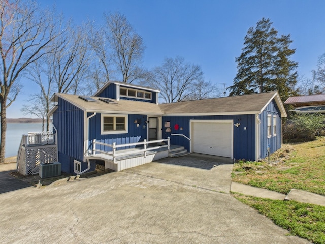 view of front facade with central air condition unit, concrete driveway, an attached garage, board and batten siding, and a deck with water view