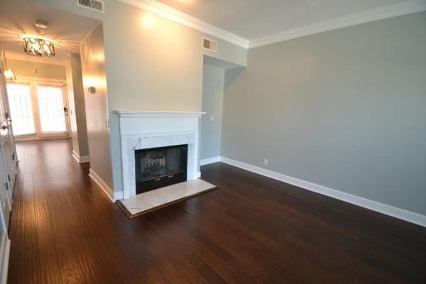 unfurnished living room with dark wood-type flooring, a premium fireplace, visible vents, baseboards, and crown molding