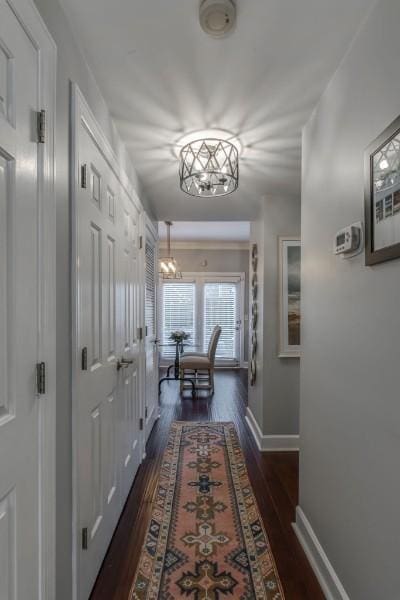 corridor with baseboards, a chandelier, and dark wood finished floors