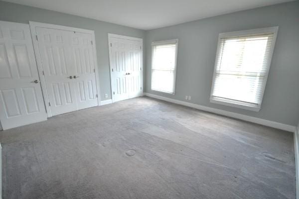 unfurnished bedroom featuring carpet floors, baseboards, and two closets