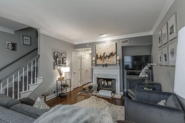 living area with crown molding, visible vents, a high end fireplace, wood finished floors, and stairs