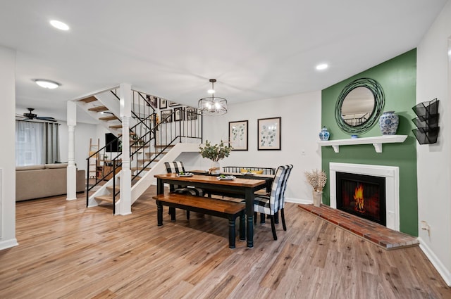 dining room with wood finished floors, a lit fireplace, baseboards, and stairs