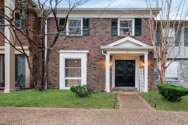 view of front of property with french doors, brick siding, and a front lawn