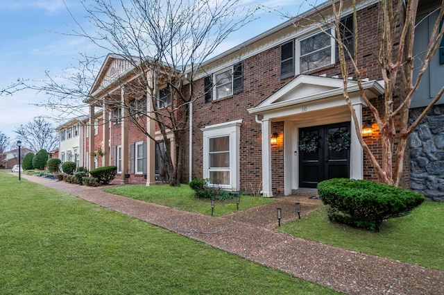 view of front of property with french doors, brick siding, and a front lawn