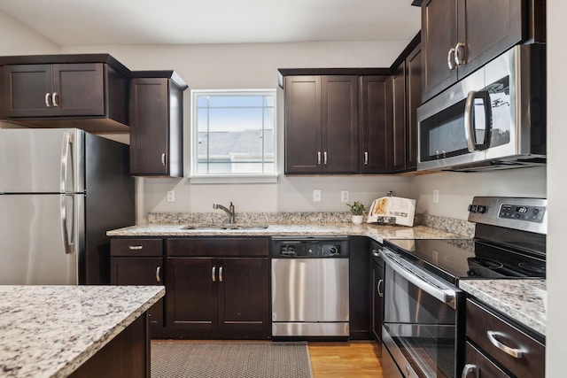 kitchen featuring appliances with stainless steel finishes, light wood-type flooring, a sink, and dark brown cabinets