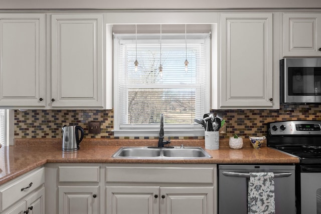 kitchen with appliances with stainless steel finishes, white cabinetry, a sink, and tasteful backsplash