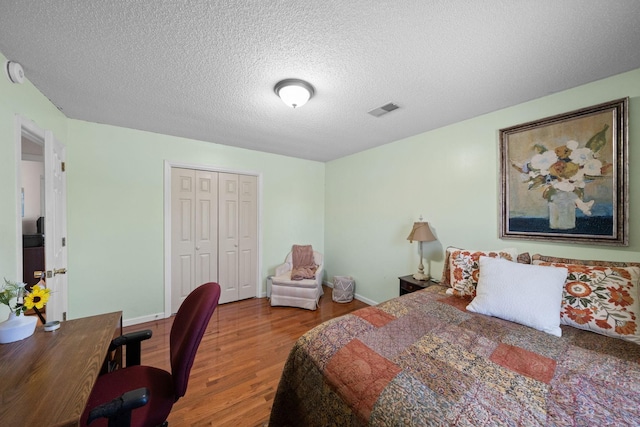 bedroom featuring baseboards, visible vents, wood finished floors, a textured ceiling, and a closet