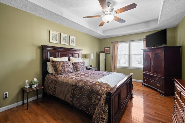 bedroom with a tray ceiling, a textured ceiling, baseboards, and wood finished floors