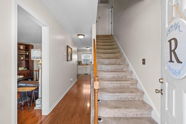 stairs featuring baseboards, visible vents, a textured ceiling, and wood finished floors