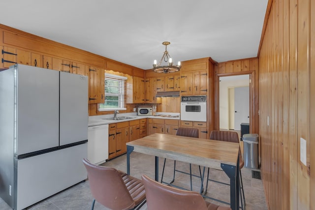 kitchen featuring pendant lighting, a notable chandelier, light countertops, a sink, and white appliances