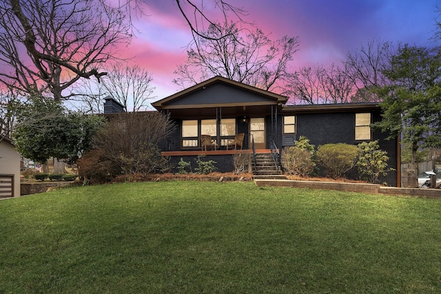 view of front facade featuring covered porch, brick siding, a yard, and a chimney