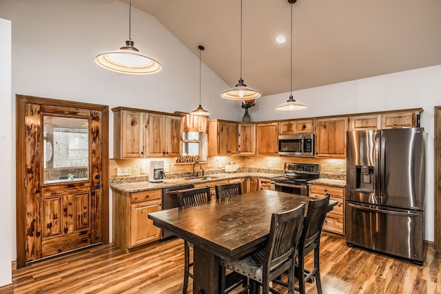 kitchen with appliances with stainless steel finishes, a sink, light wood-style flooring, and tasteful backsplash