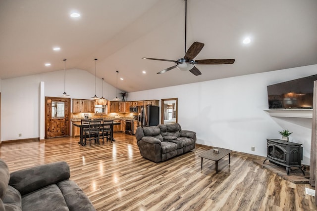 living area with ceiling fan, high vaulted ceiling, recessed lighting, light wood-style floors, and a wood stove