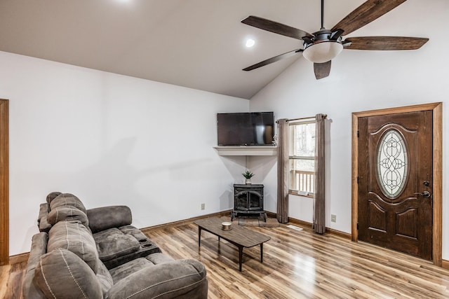 living room featuring ceiling fan, wood finished floors, baseboards, vaulted ceiling, and a wood stove