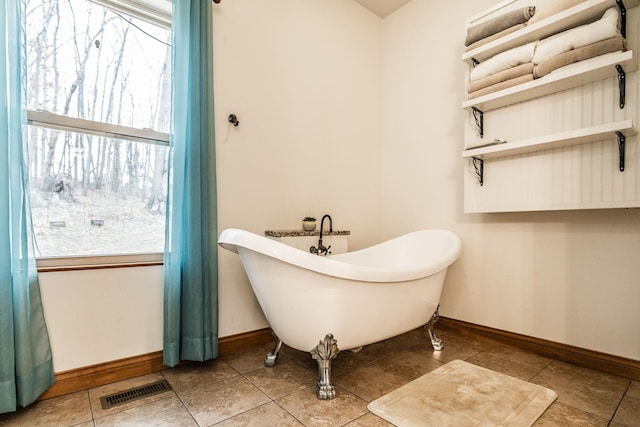 bathroom with visible vents, a freestanding tub, a wealth of natural light, and baseboards