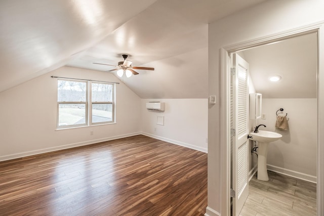 bathroom featuring lofted ceiling, ceiling fan, a wall unit AC, wood finished floors, and baseboards