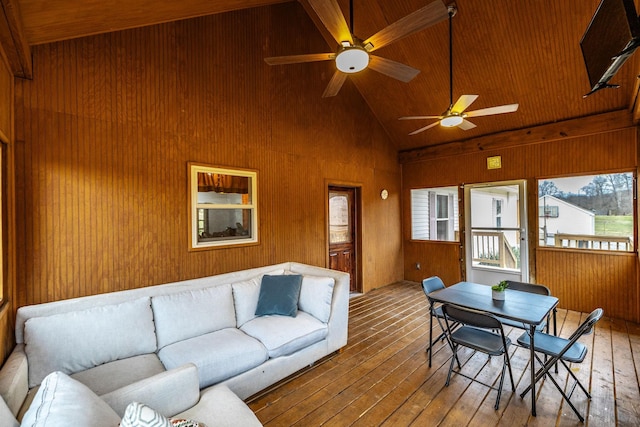 living area featuring high vaulted ceiling, wood-type flooring, a ceiling fan, and wooden walls