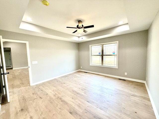 empty room with a ceiling fan, visible vents, baseboards, light wood-type flooring, and a tray ceiling