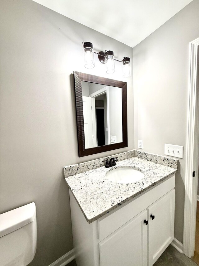 half bath with toilet, baseboards, and vanity