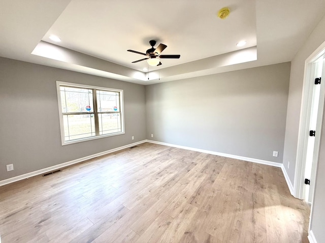 empty room featuring ceiling fan, visible vents, light wood-style floors, baseboards, and a raised ceiling