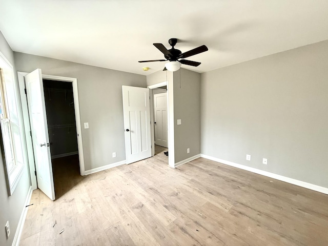 unfurnished bedroom with a ceiling fan, a walk in closet, baseboards, and light wood finished floors