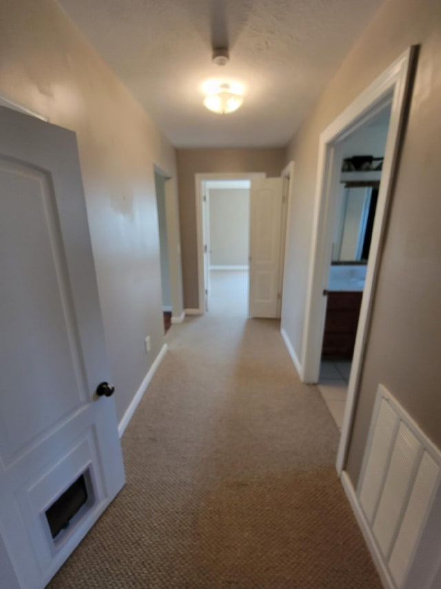 hallway with light colored carpet, visible vents, and baseboards