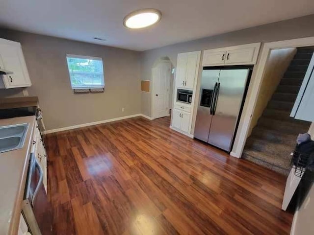 kitchen featuring wood finished floors, white cabinets, stainless steel fridge with ice dispenser, built in microwave, and baseboards