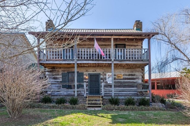 view of front of home featuring metal roof, a chimney, and a balcony