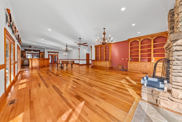 unfurnished living room featuring visible vents, a stone fireplace, light wood finished floors, and ceiling fan with notable chandelier