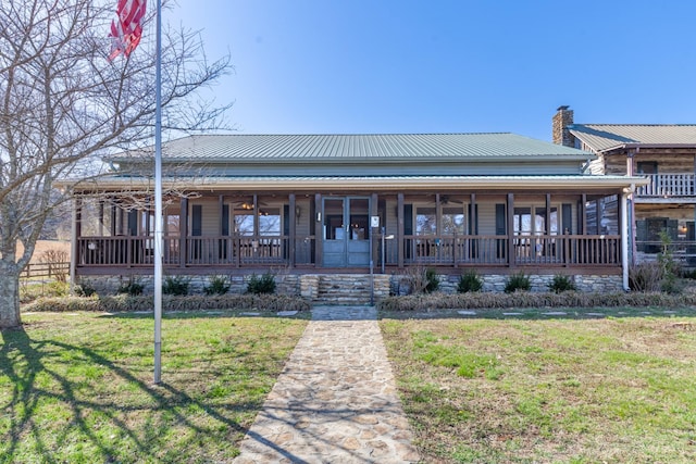 farmhouse-style home with a chimney, covered porch, a ceiling fan, a front yard, and metal roof