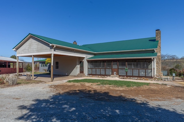 view of front facade with a sunroom, a chimney, metal roof, and a carport