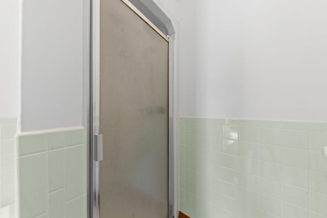 full bathroom featuring a wainscoted wall, a shower stall, and tile walls