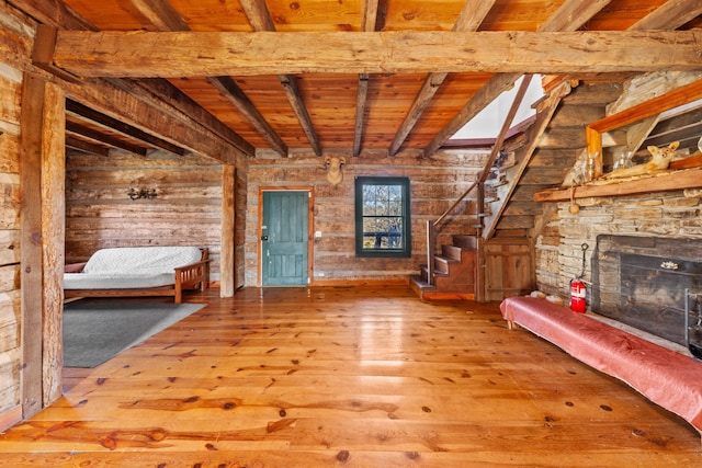 unfurnished living room featuring wooden ceiling, beamed ceiling, wood finished floors, stairs, and a stone fireplace