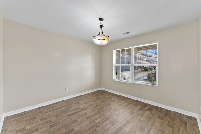 spare room featuring baseboards, visible vents, and wood finished floors