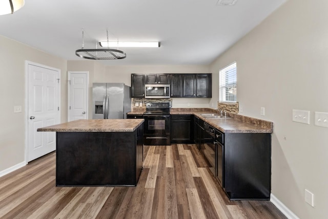 kitchen featuring a center island, a sink, black appliances, wood finished floors, and baseboards