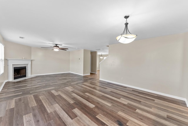 unfurnished living room with wood finished floors, a ceiling fan, a fireplace with flush hearth, visible vents, and baseboards