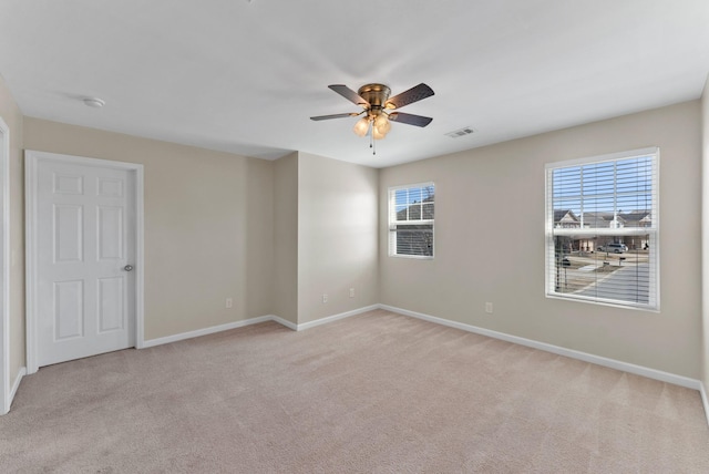 spare room with light carpet, ceiling fan, visible vents, and baseboards