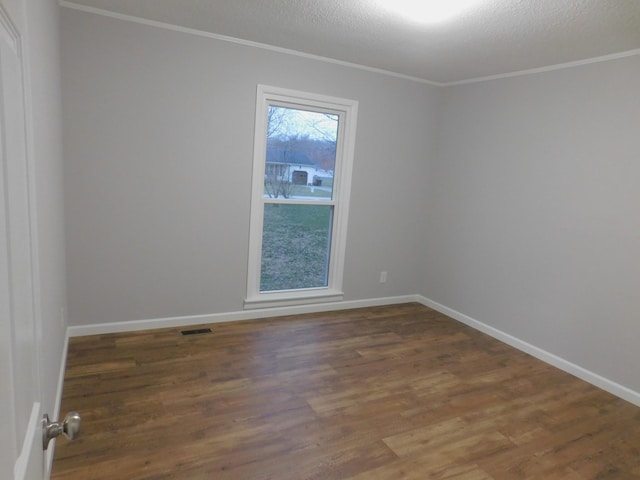 empty room featuring visible vents, ornamental molding, a textured ceiling, wood finished floors, and baseboards