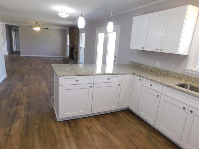 kitchen with decorative light fixtures, a peninsula, a fireplace, white cabinets, and dark wood-style flooring