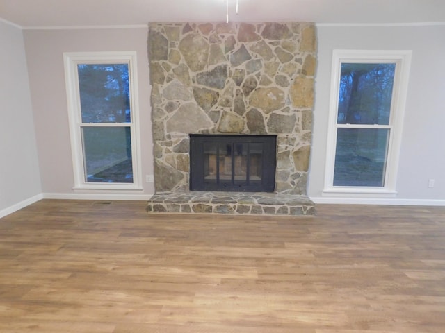 unfurnished living room with a stone fireplace, wood finished floors, baseboards, and ornamental molding