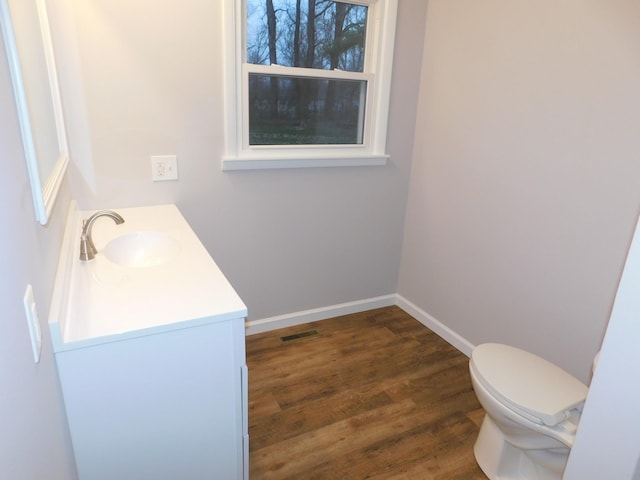 half bathroom featuring vanity, wood finished floors, baseboards, visible vents, and toilet